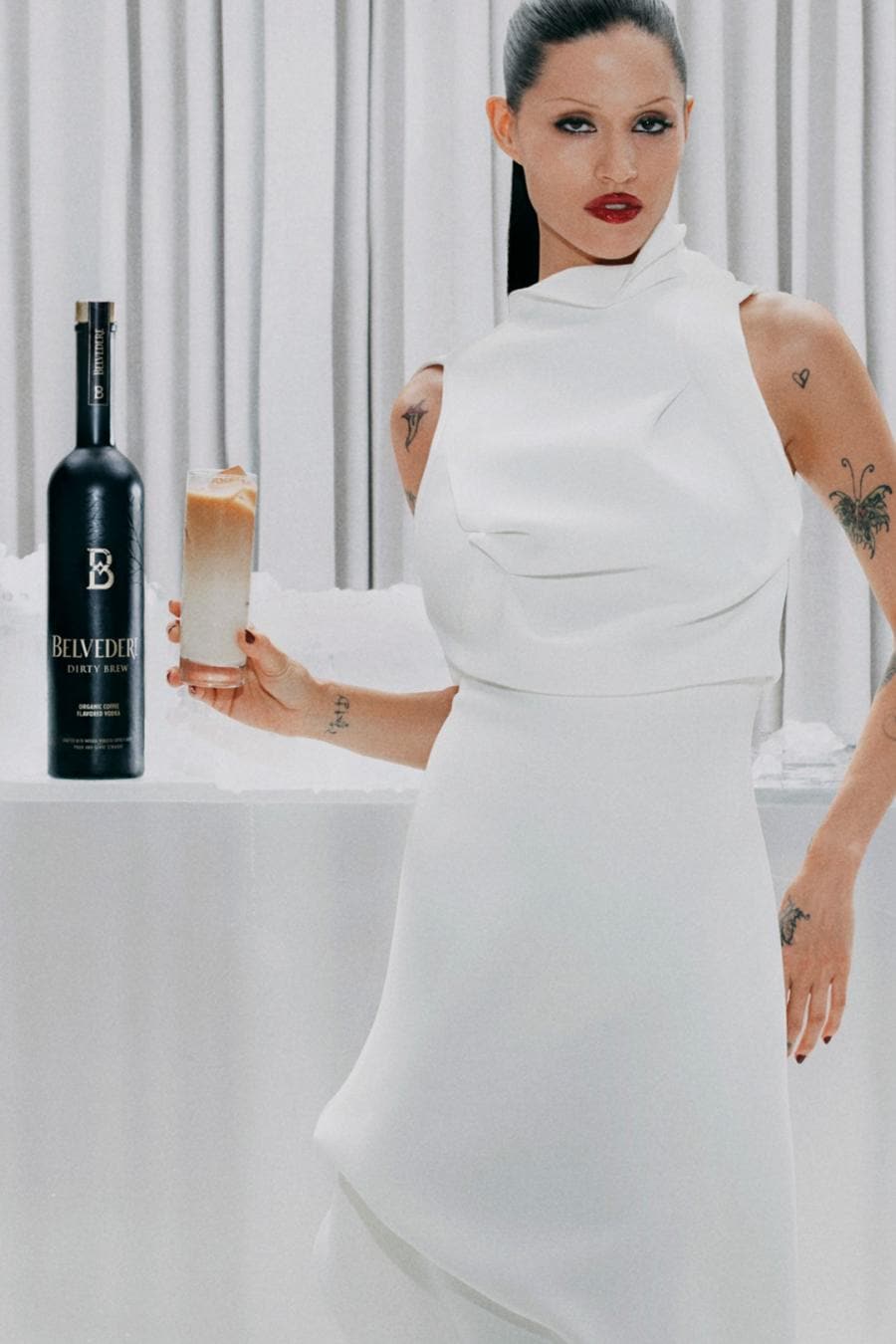 Gabbriette in a white dress holding a Dirty Latte next to a bottle of Belvedere Dirty Brew