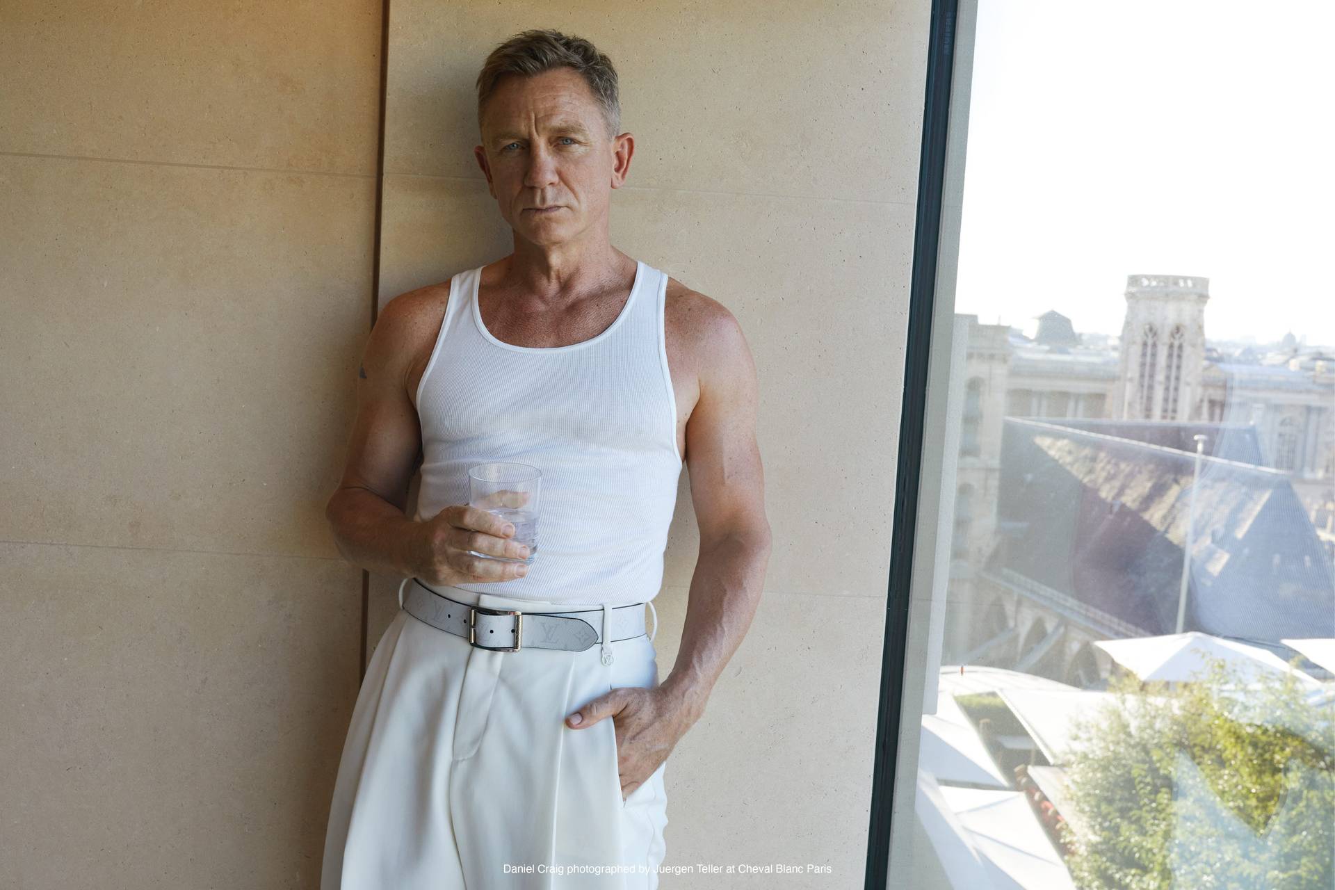 daniel craig standing near a window wearing white holding a cocktail